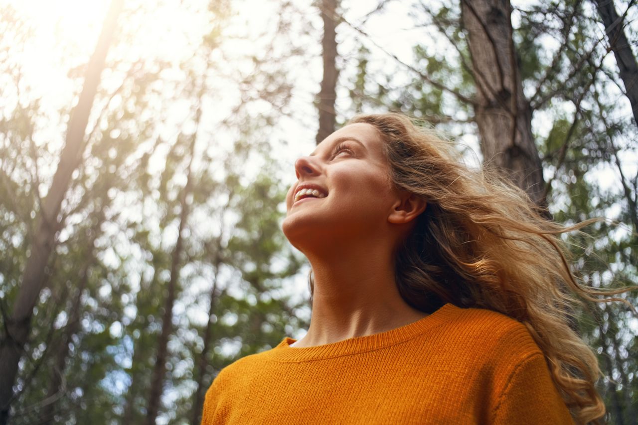 Una joven sonríe mientras disfruta de la luz del sol en un bosque