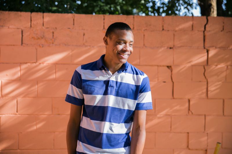 Un joven de pie contra una pared de ladrillos color naranja