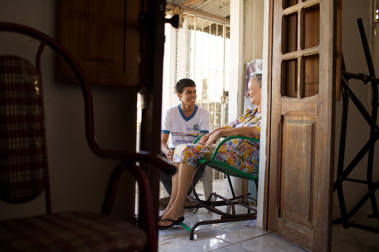 Un joven sentado en la entrada de una casa con una mujer mayor mientras charlan y disfrutan del evangelio de Jesucristo