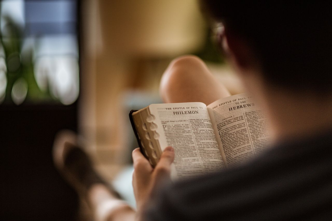 Un hombre sentado en un sofá estudia la Santa Biblia con las páginas abiertas en la epístola de Pablo a Filemón